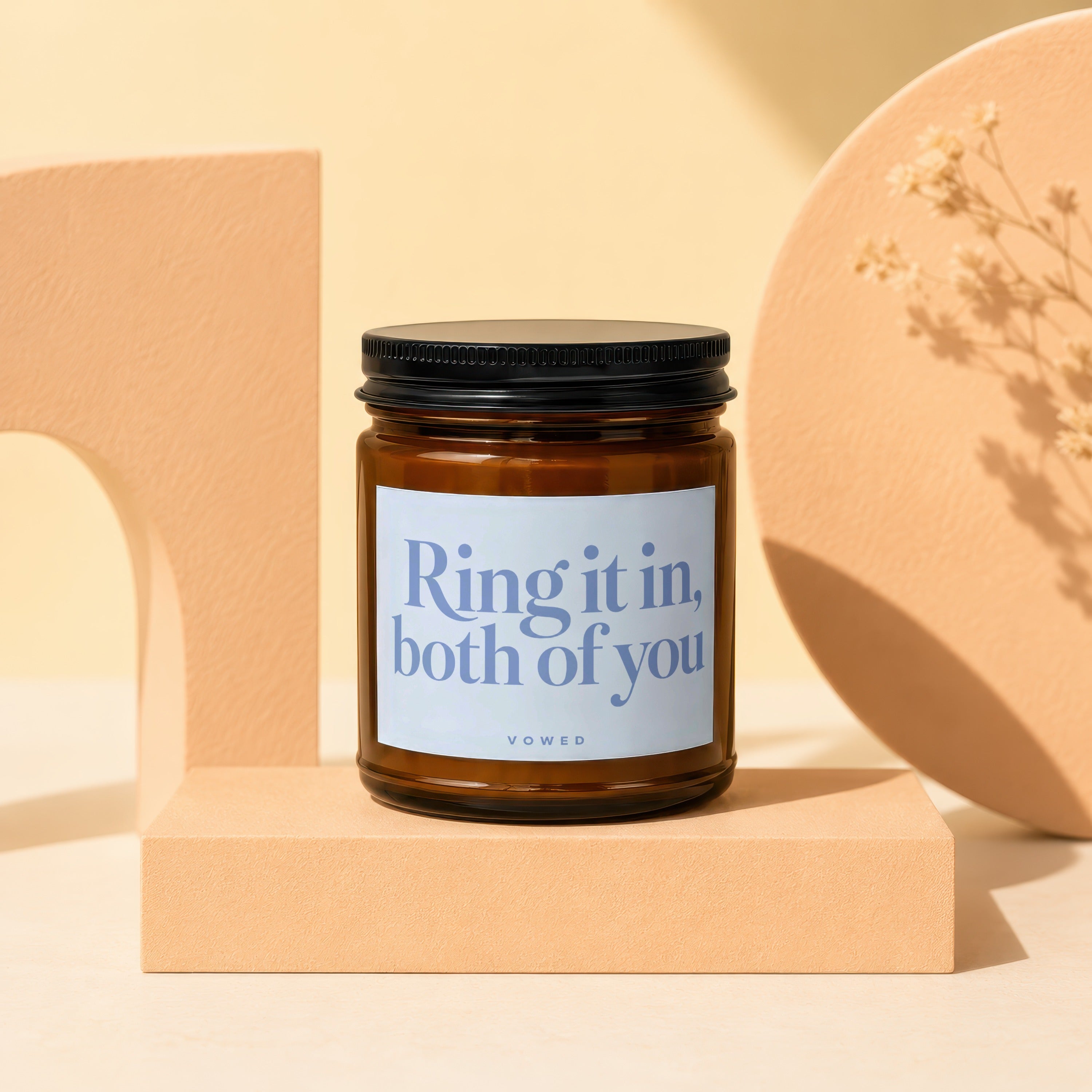 Amber jar candle with black lid, reads "Ring it in, both of you" on label.