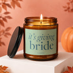 Amber jar candle with lit wick, reads "it's giving bride" VOWED.
