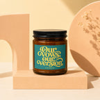 Amber glass candle with "Our Vows, Our Version" label, in front of decorative objects.