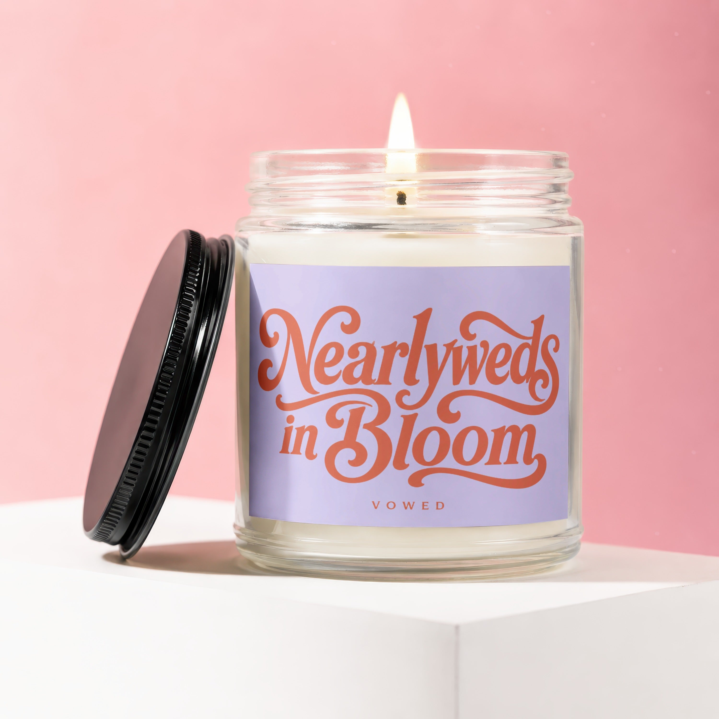 Glass candle labeled "Nearlyweds in Bloom" by VOWED, with lit wick.