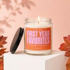 Glass candle with orange label reading "YEAR ONE: FIRST YEAR FAVORITES", lit wick.