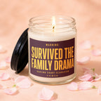 Glass candle with lit wick and label reading "WARNING: SURVIVED THE FAMILY DRAMA"
