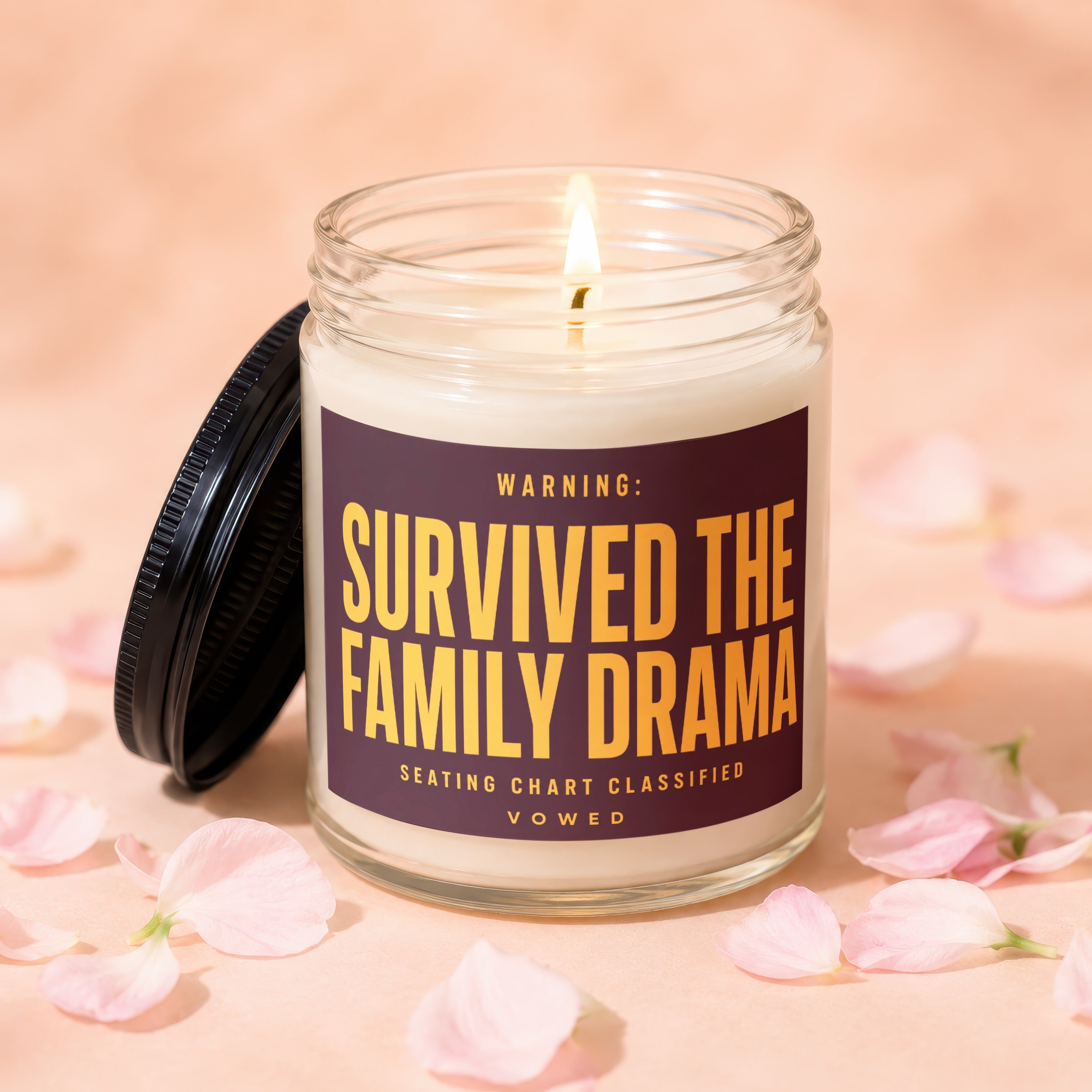 Glass candle with lit wick and label reading "WARNING: SURVIVED THE FAMILY DRAMA"