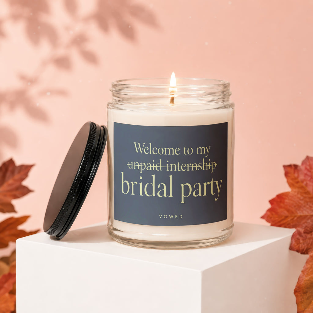 Glass candle with dark label reading "Welcome to my unpaid internship bridal party VOWED".