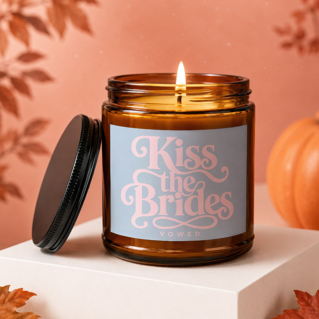 Amber glass candle with "Kiss the Brides VOWED" text and lit flame.