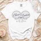 A white t-shirt featuring a custom seashell illustration with the text "Olivia's Bachelorette Miami Beach Est. 2027."