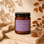 Amber glass candle with black lid, label reads "Love, Laughter & Happily Ever After".