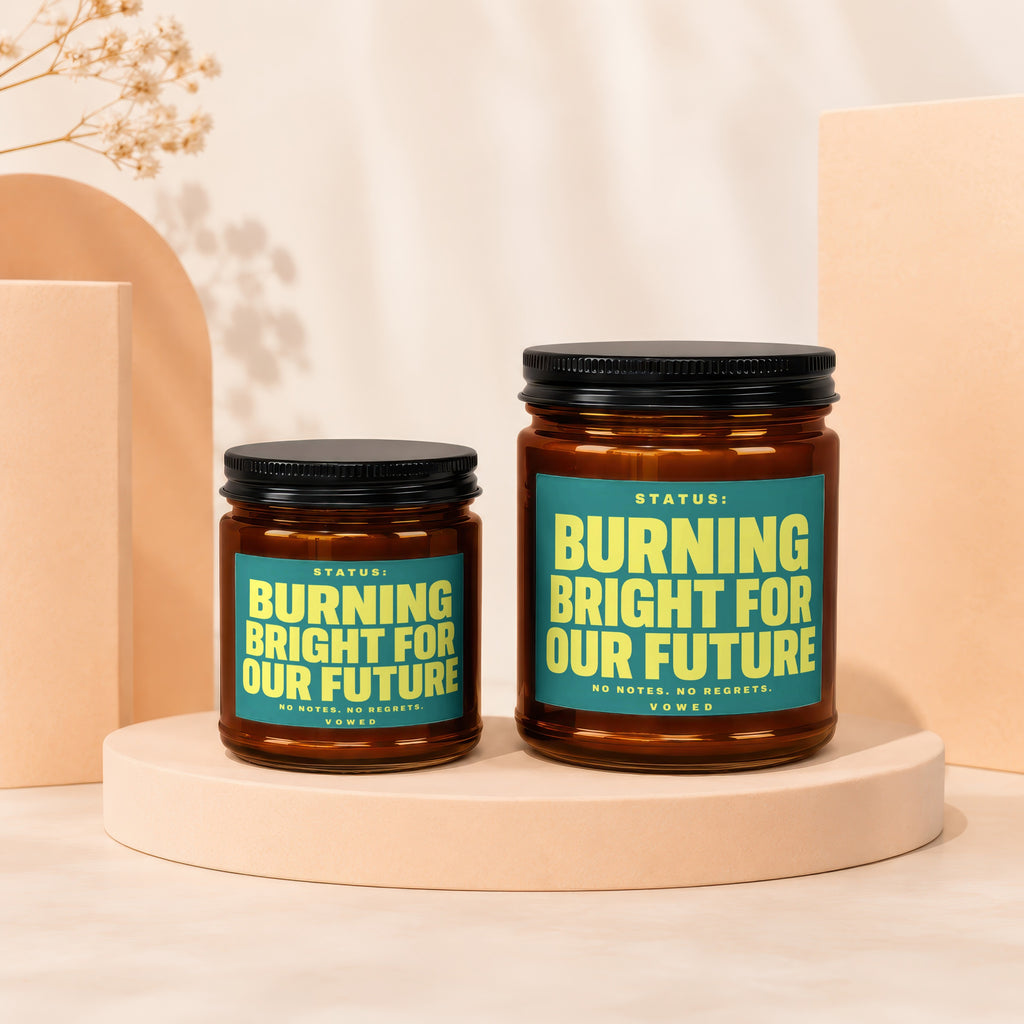Two amber glass candles with teal labels reading "Burning Bright For Our Future."