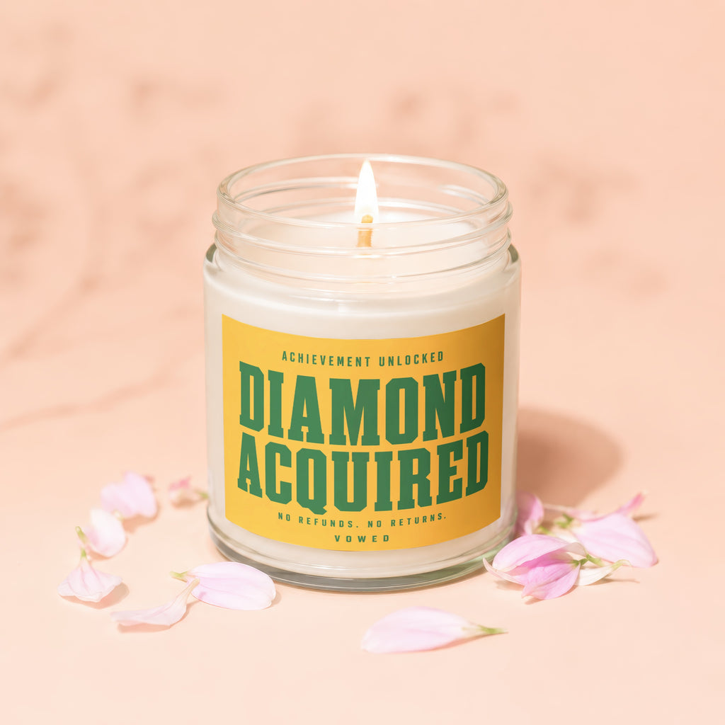 Candle with yellow label reading "DIAMOND ACQUIRED" surrounded by pink petals.