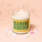 Candle with yellow label reading "DIAMOND ACQUIRED" surrounded by pink petals.