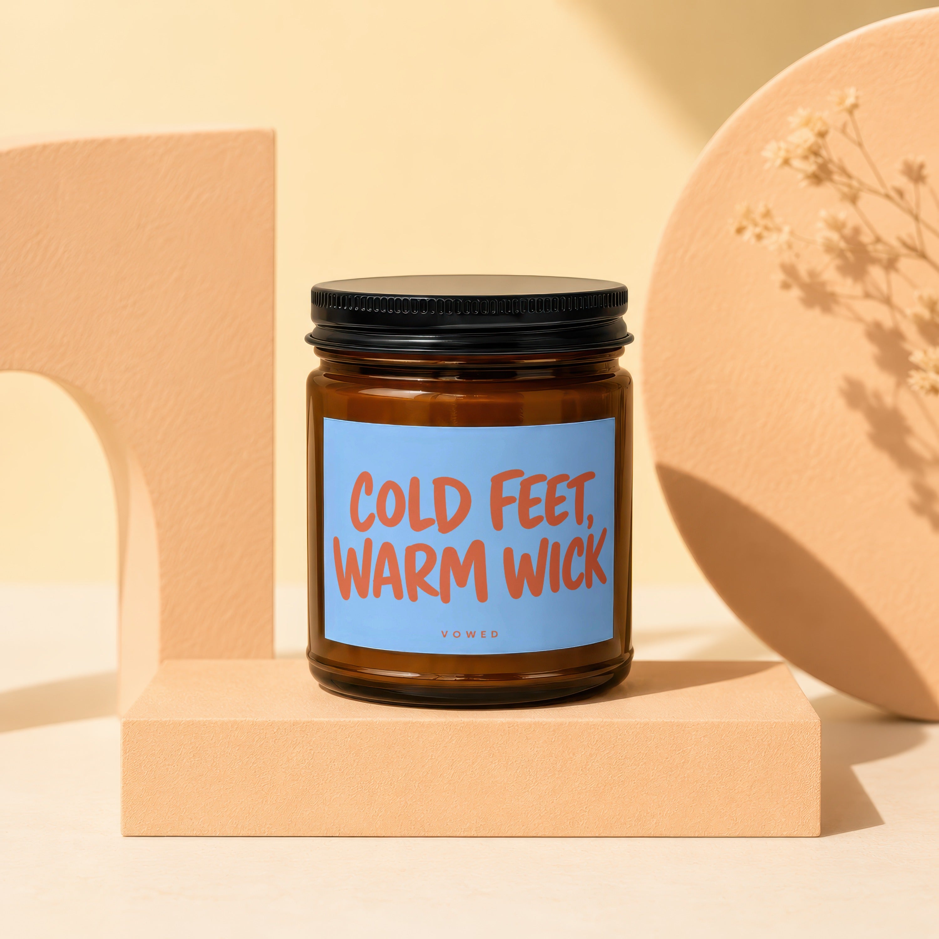 Brown glass candle with blue label reading "COLD FEET, WARM WICK" by VOWED.