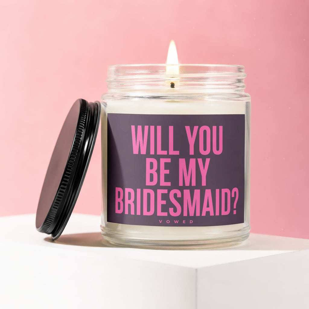 Jar candle with lit wick and dark lid, reads "Will You Be My Bridesmaid?"
