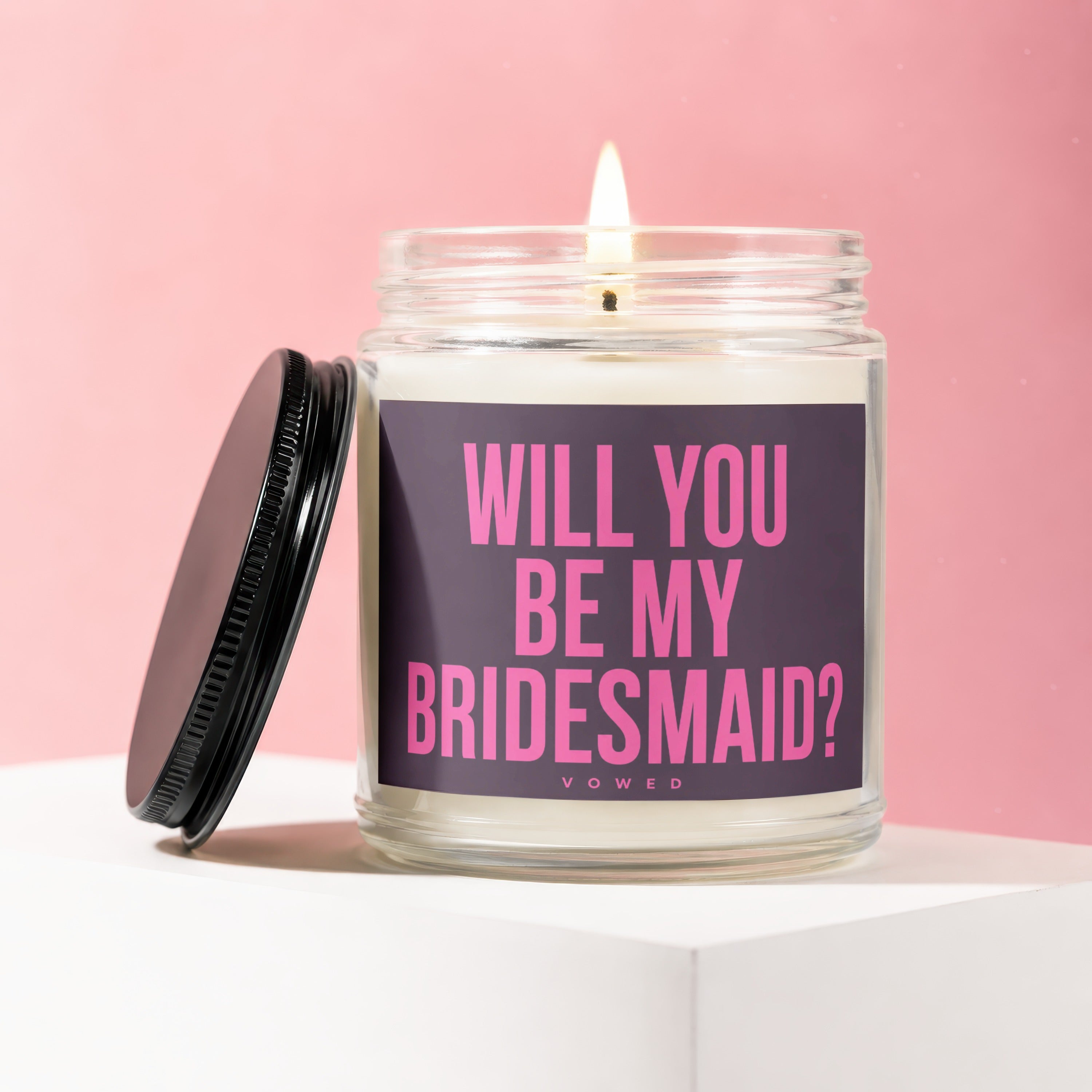 Jar candle with lit wick and dark lid, reads "Will You Be My Bridesmaid?"
