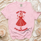 Pink t-shirt with graphic of woman crying, holding a drink, with text "OFF TO CRY AT MY SON'S WEDDING".
