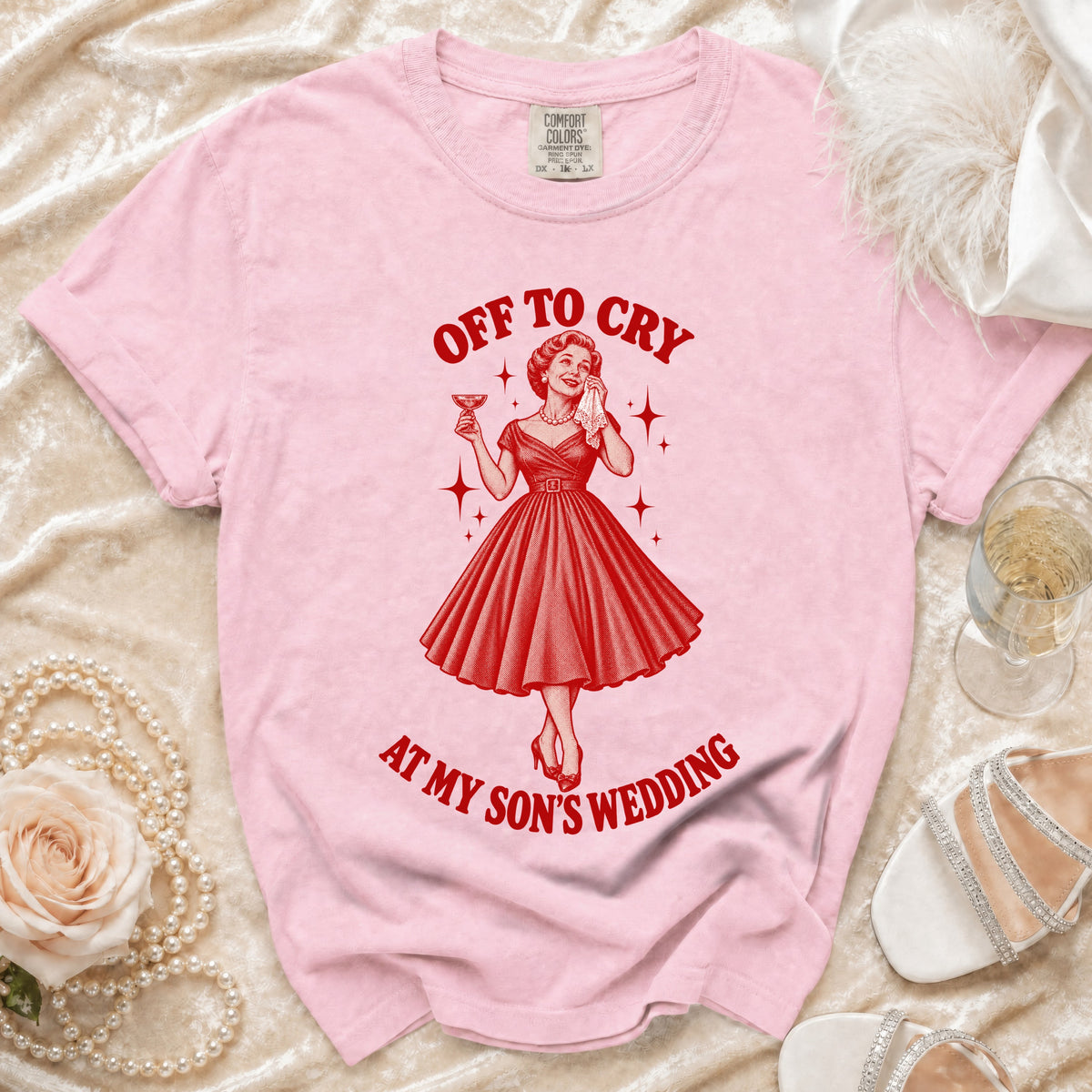 Pink t-shirt with graphic of woman crying, holding a drink, with text "OFF TO CRY AT MY SON'S WEDDING".