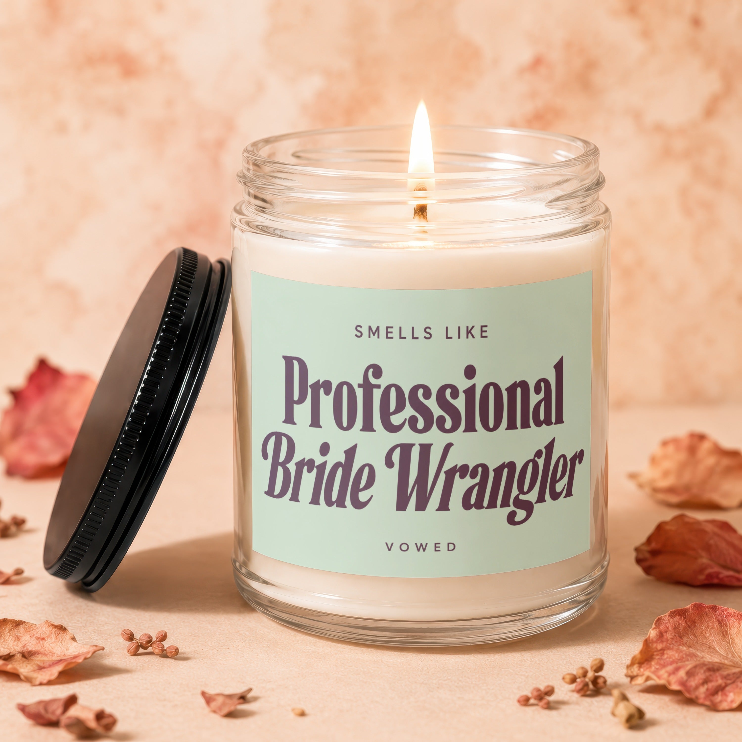 Candle with lit wick and lid beside it, reads "Smells Like Professional Bride Wrangler".