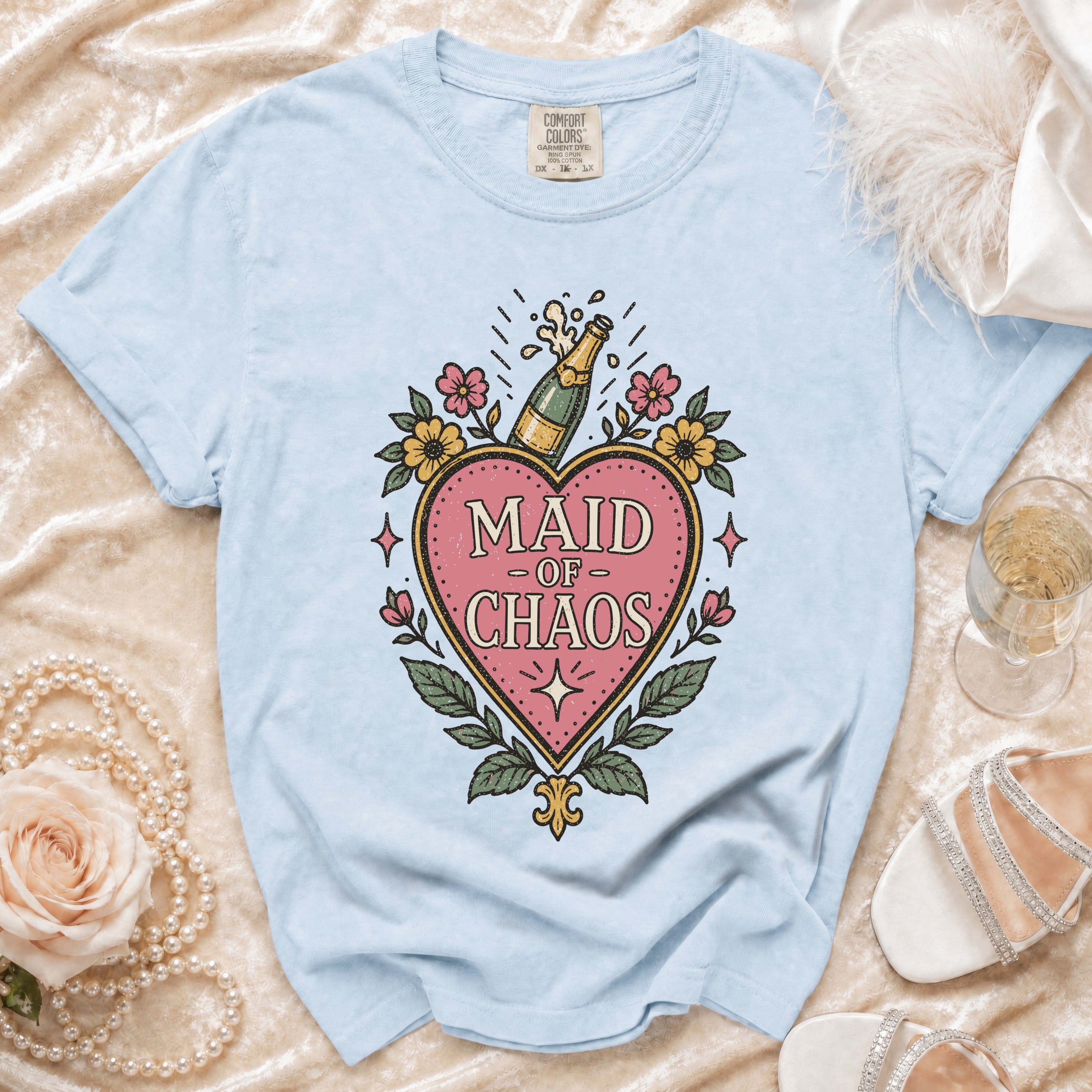 Light blue t-shirt with "Maid of Chaos" text and champagne bottle graphic.