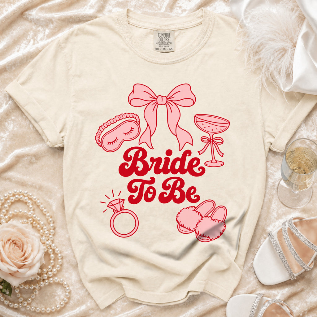 Cream t-shirt with "Bride To Be" text and bridal icons in pink.