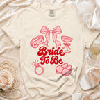 Cream t-shirt with "Bride To Be" text and bridal icons in pink.