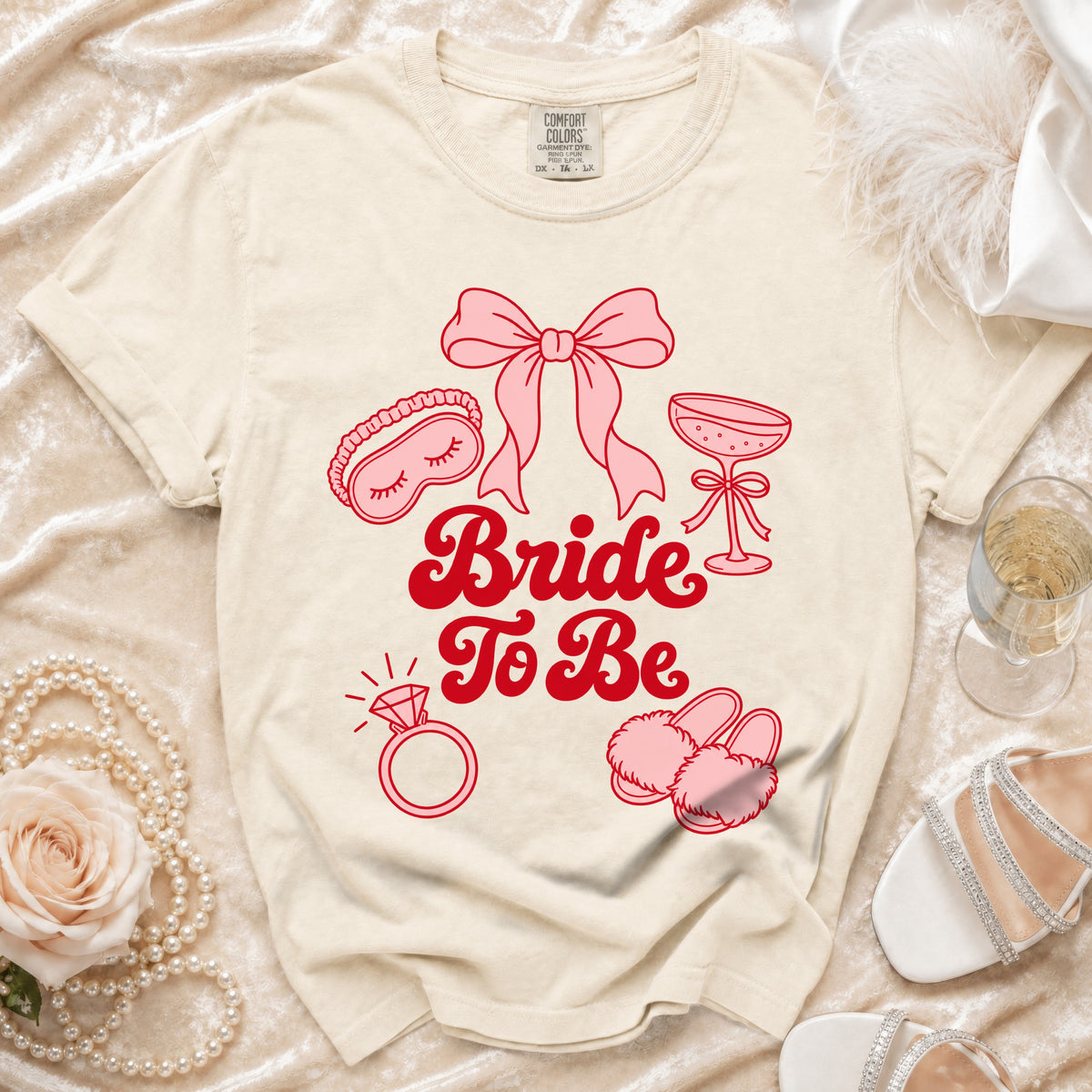 Cream t-shirt with "Bride To Be" text and bridal icons in pink.