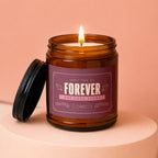 Amber candle with "Forever One Love Story" label, lid off, lit flame.