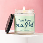 Jar candle with lit wick and black lid, labeled "Two Peas in a Pod Vowed | Hand Poured".