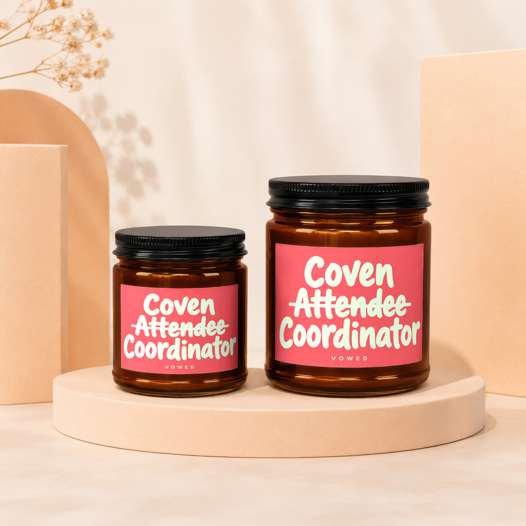 Two brown glass candles with pink labels reading "Coven Attendee Coordinator" and "VOWED".