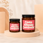 Two brown glass candles with pink labels reading "Coven Attendee Coordinator" and "VOWED".