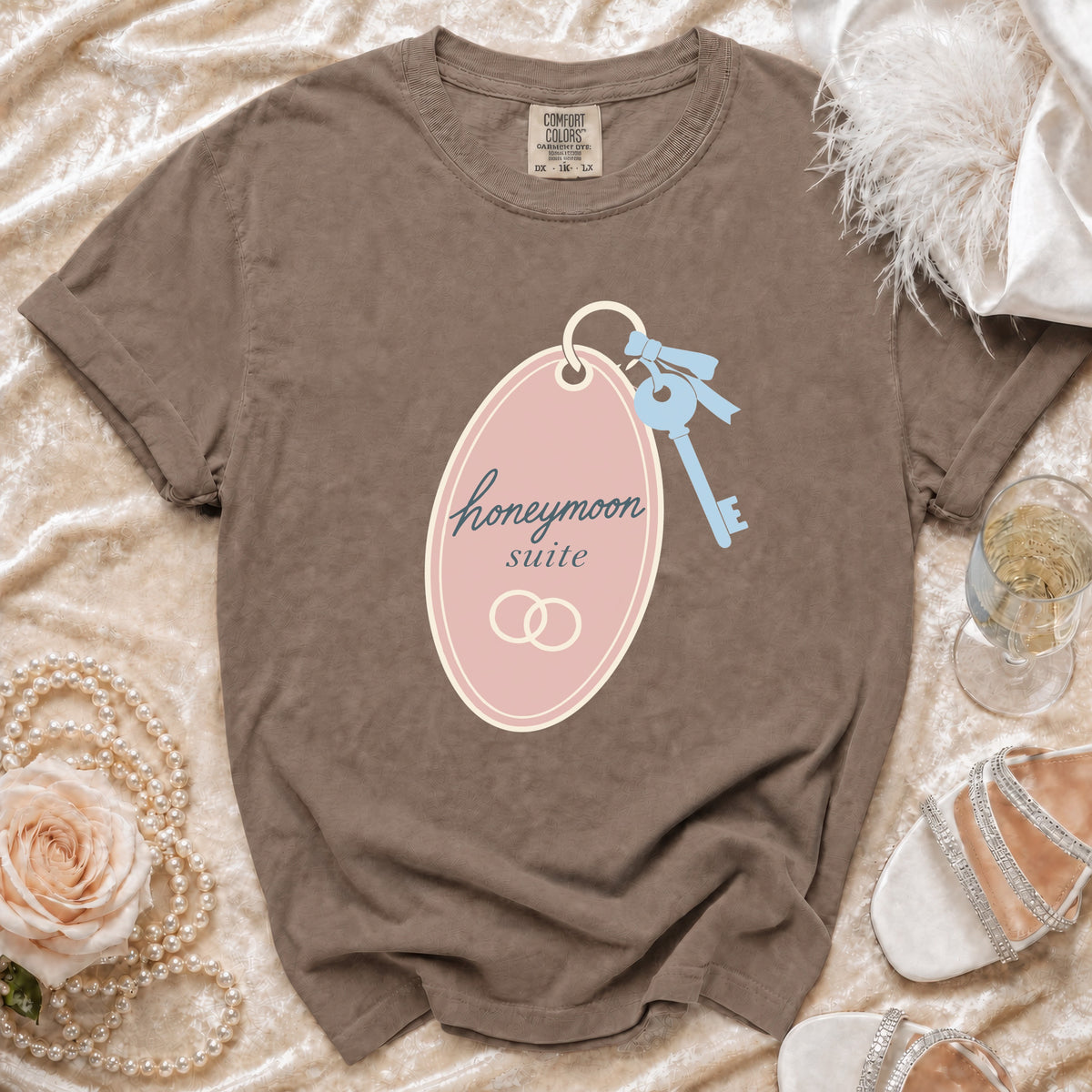 Brown t-shirt with "honeymoon suite" graphic, pearl necklace, and white heels.