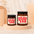 Two amber glass jars with black lids, labels read "SHE SAID YES".
