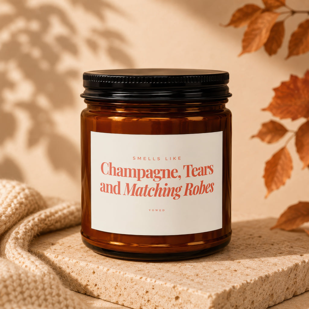 Amber candle with black lid labeled "Smells Like Champagne, Tears and Matching Robes"