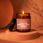 Amber glass candle with burning wick, reads "Light Me When I Tell The Proposal Story Again".