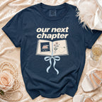 Navy t-shirt with "our next chapter" text over an open book graphic.