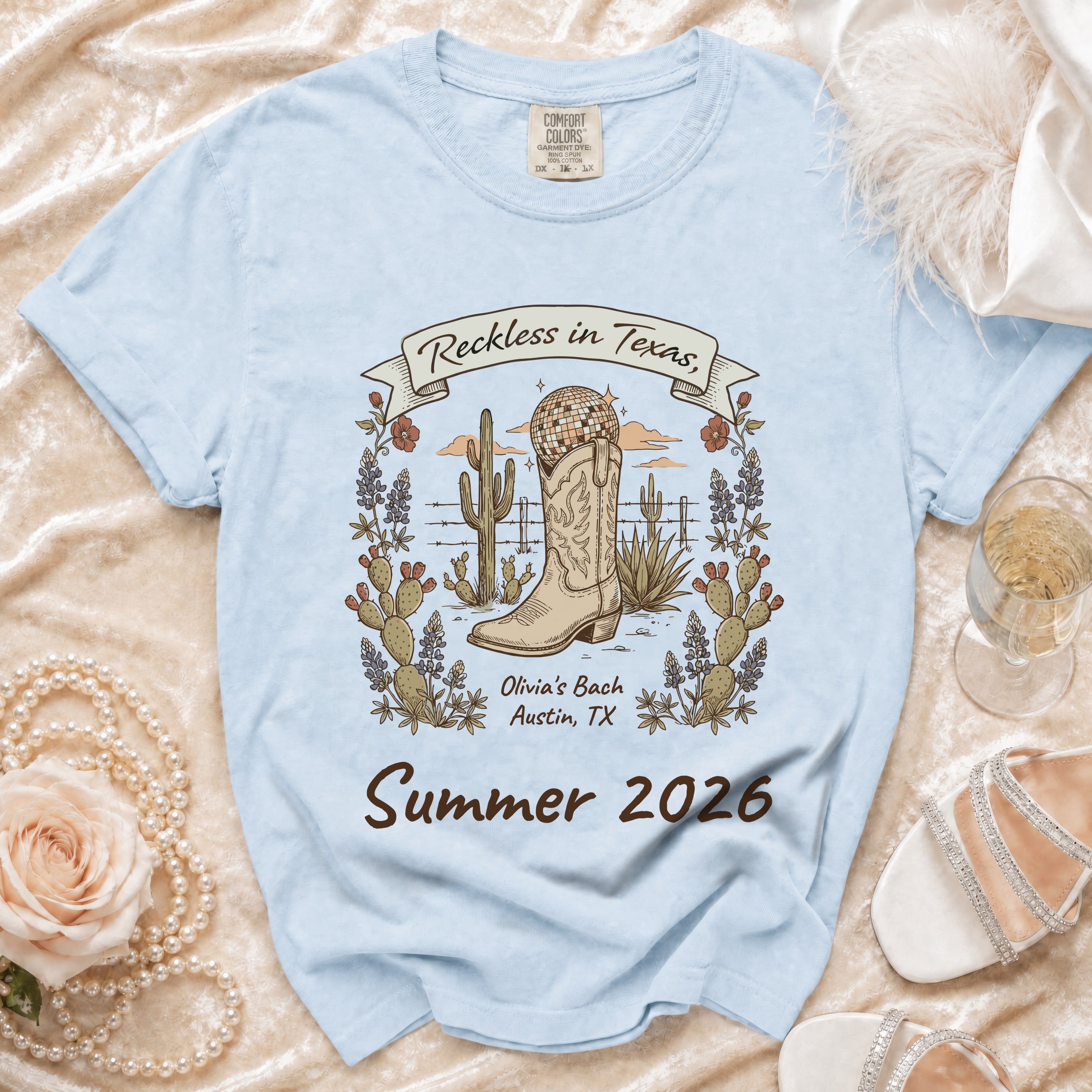 Light blue t-shirt with cowboy boot, cactus, and text "Reckless in Texas, Olivia's Bach Summer 2026".