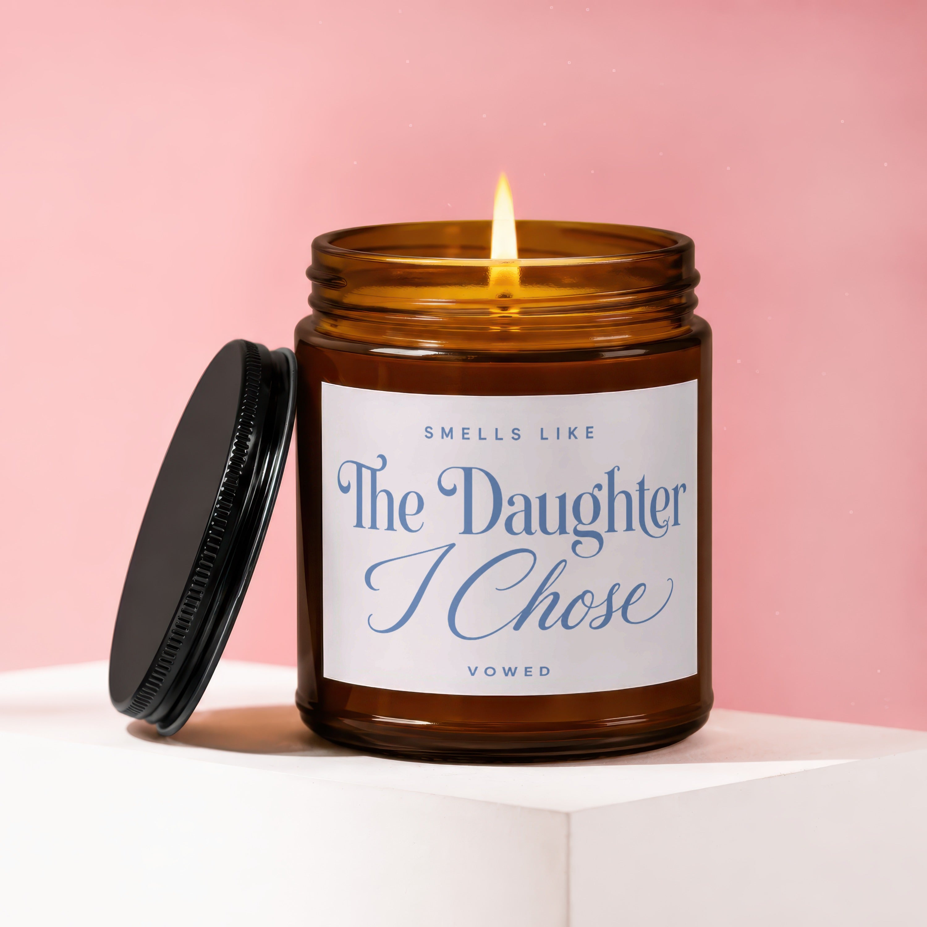 Amber glass candle with a lit wick and white label reading "The Daughter I Chose."
