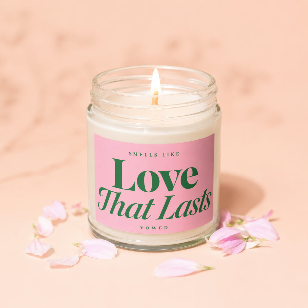 Candle labeled "Smells Like Love That Lasts Vowed" surrounded by pink petals.