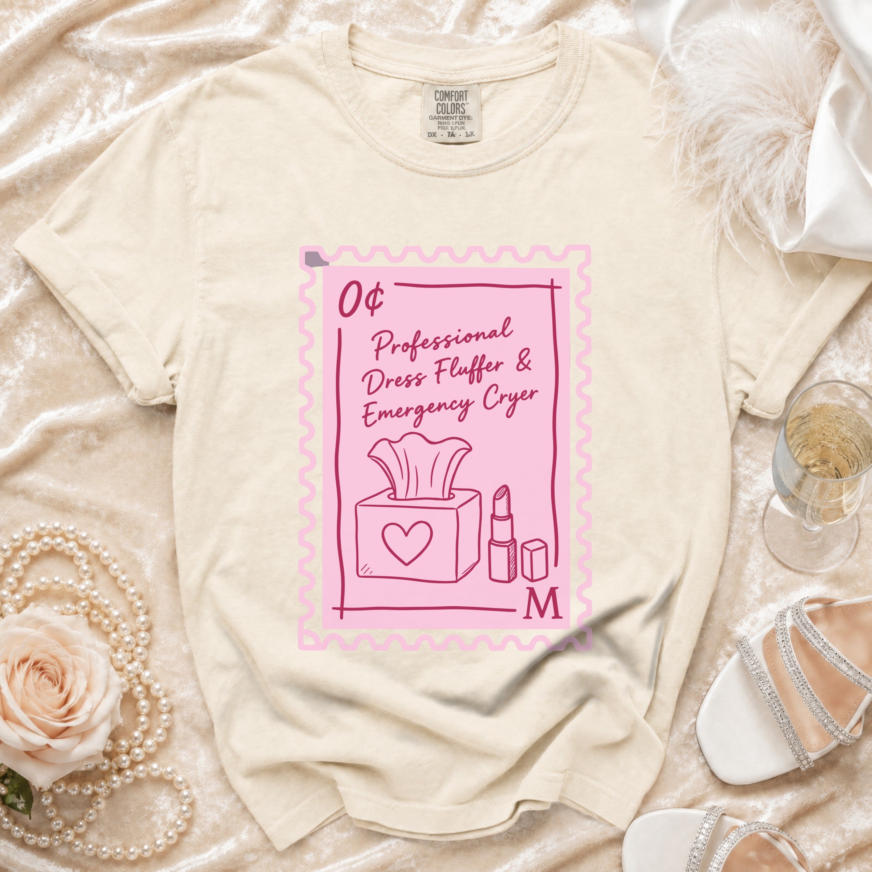 Cream t-shirt with a pink stamp graphic that says "Professional Dress Fluffer & Emergency Cryer".