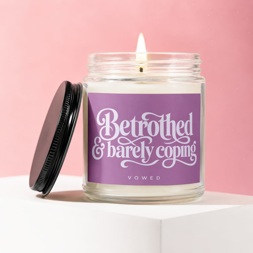 Lit candle in a glass jar with purple label reading "Betrothed & barely coping".