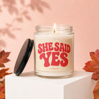 Candle with "SHE SAID YES" text on a retro-style label, lit flame.