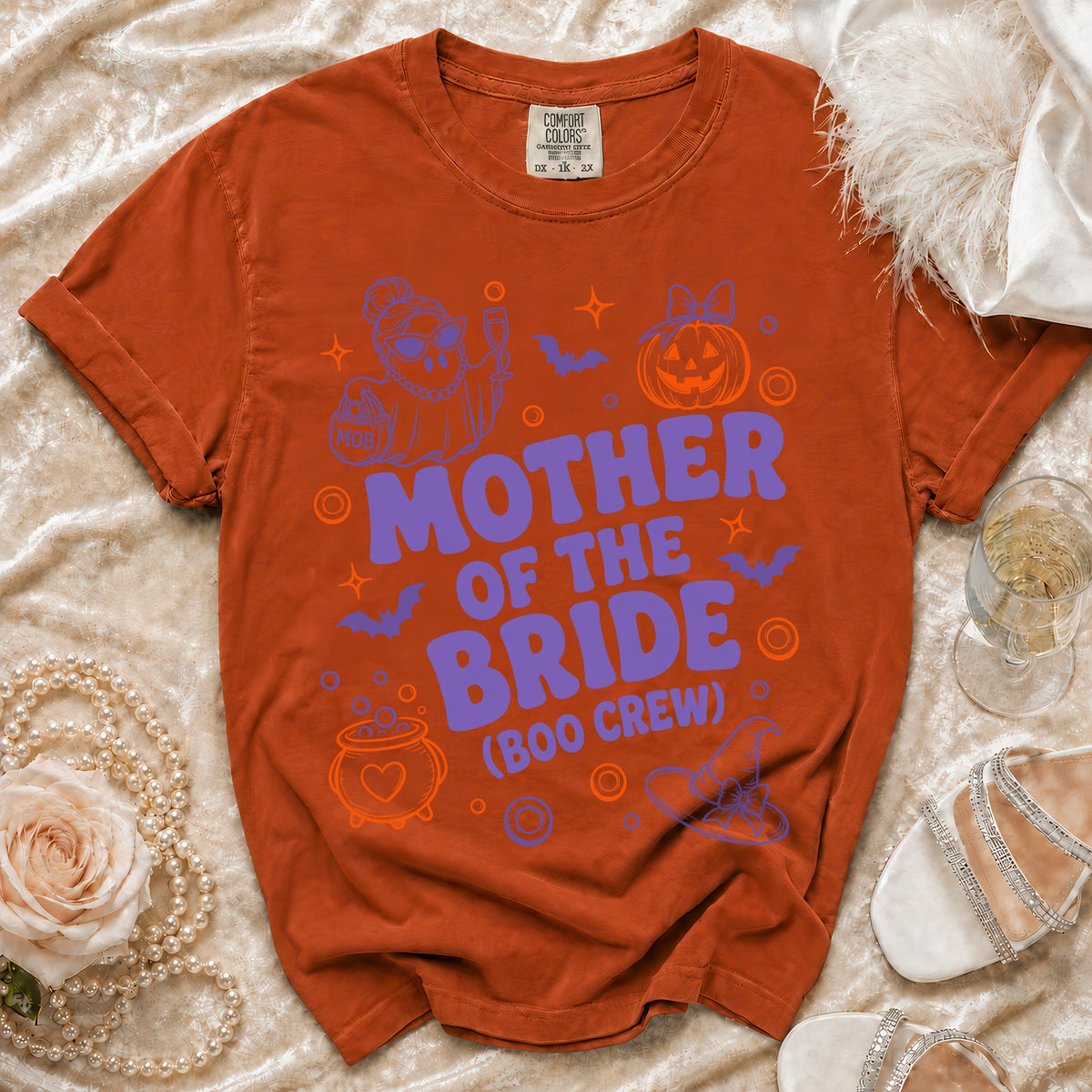 An orange crewneck t-shirt featuring a purple and orange Halloween design with the text MOTHER OF THE BRIDE BOO CREW.