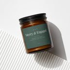 Amber glass candle with dark green label reading "Merry & Engaged" and "Vowed".