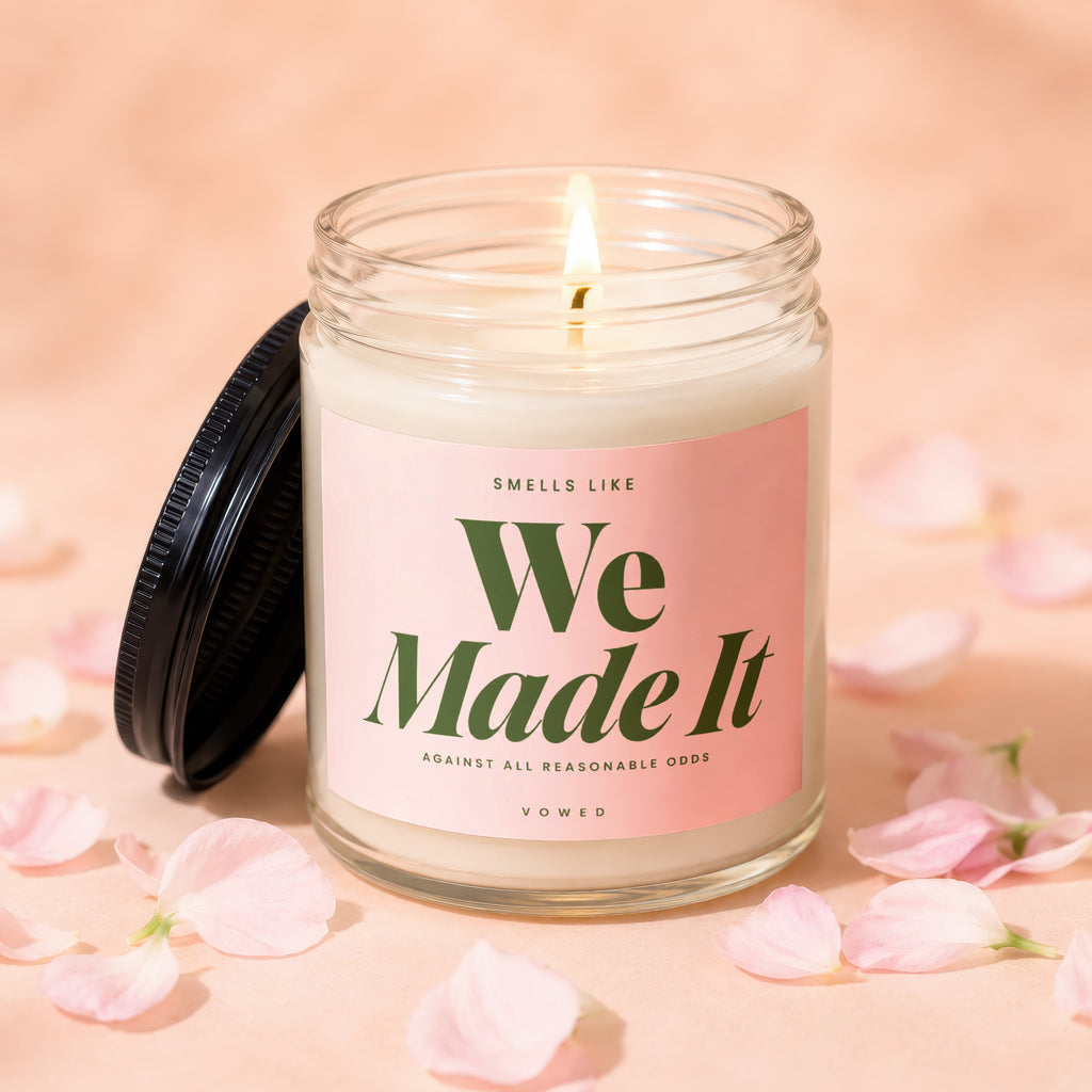 Lit candle with pink label reading "We Made It" amidst scattered petals.