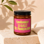 Candle with text "Emotionally Legally His Problem Now Vowed" on a pink label.