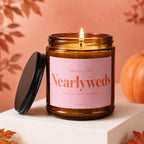 Lit amber jar candle with pink label reading "Nearlyweds", "Save the Date, Someday", "Vowed". The lid is off.