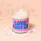 A lit candle in a glass jar with a pink label that says "LOVE, FULLY LIT"