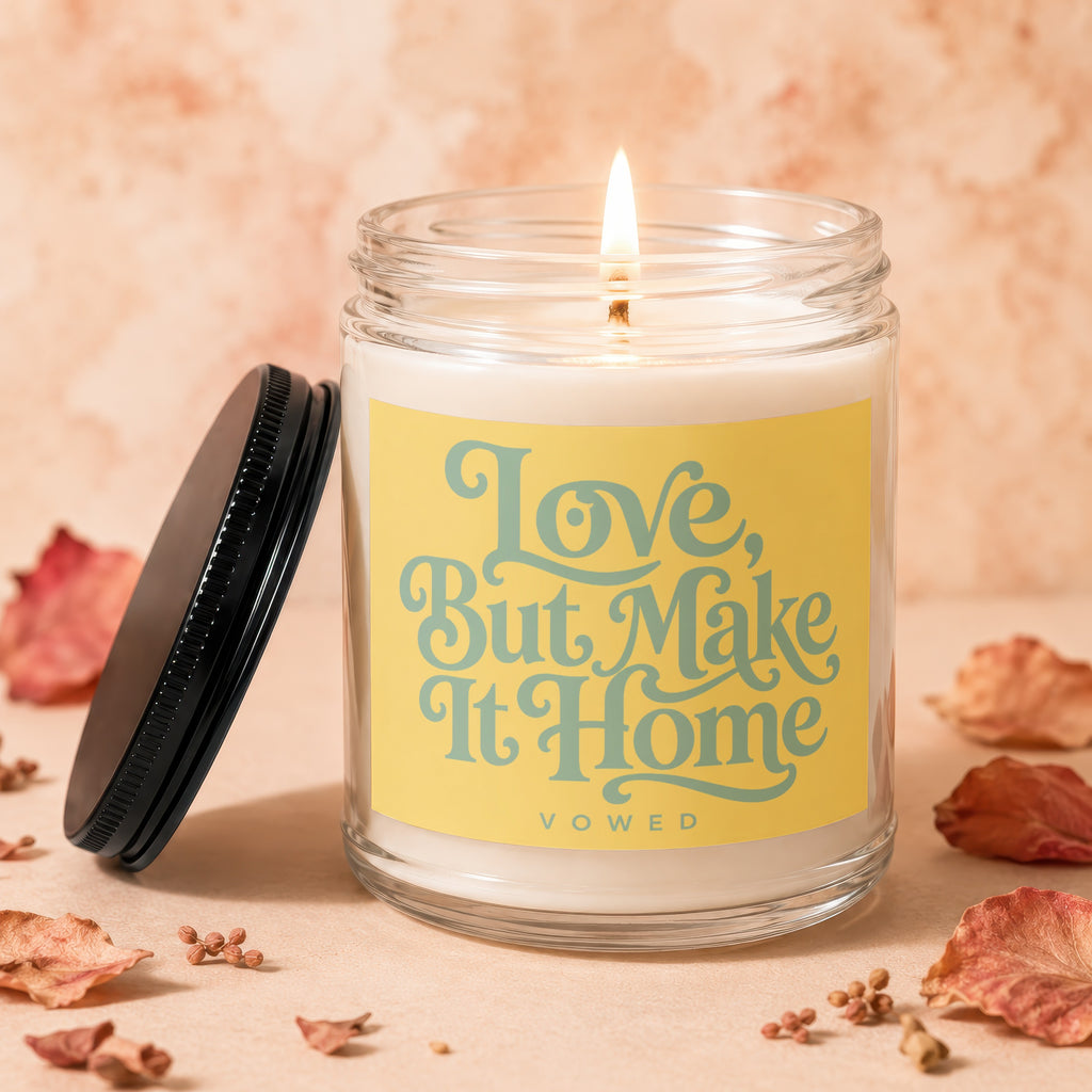Jar candle with lit flame on yellow label reading "Love, But Make It Home VOWED."