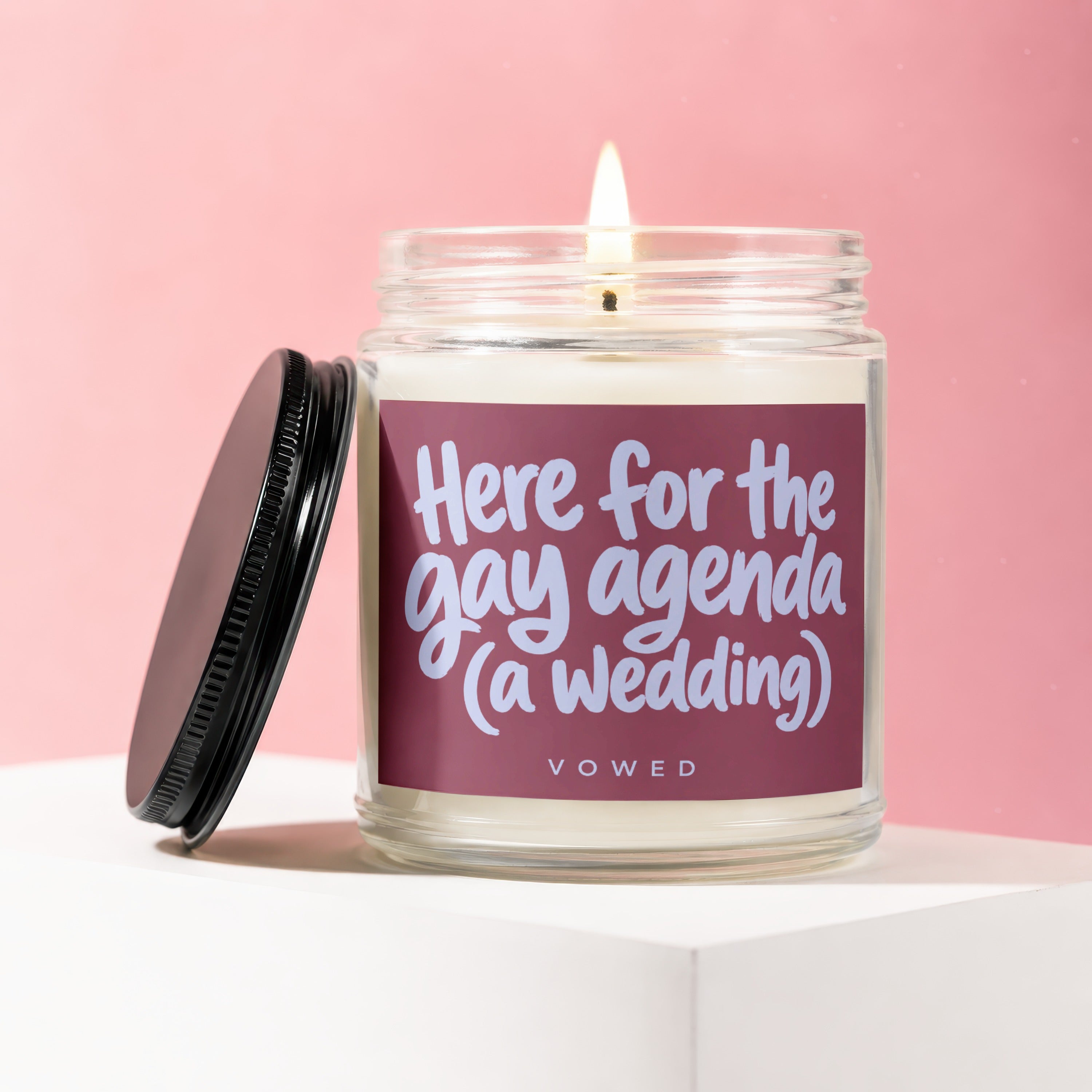 Jar candle with lit wick and label reading "Here for the gay agenda (a wedding)".