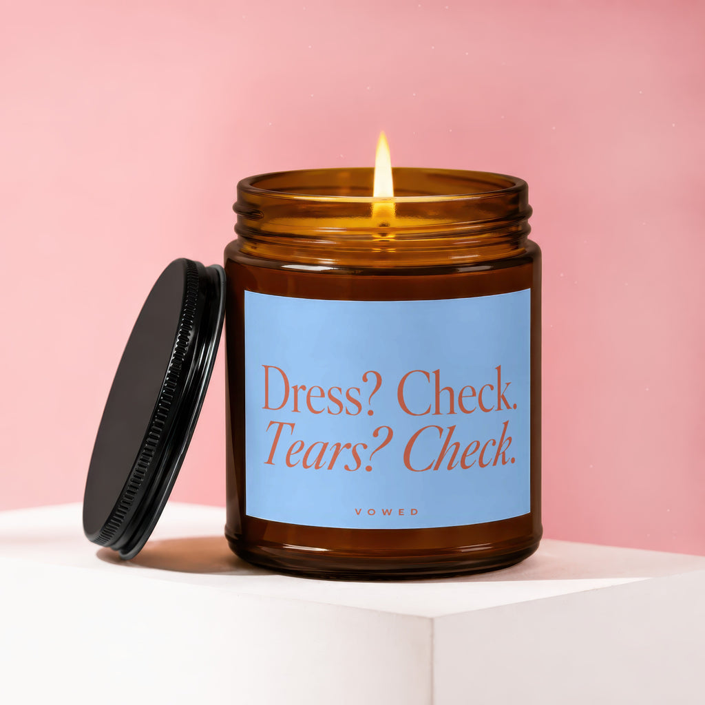Amber jar candle with lit wick and light blue label reading "Dress? Check. Tears? Check."