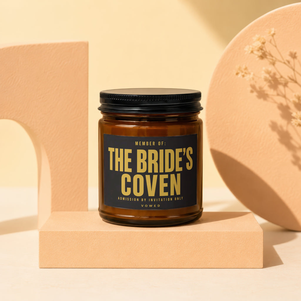 Amber candle with black label reading "MEMBER OF: THE BRIDE'S COVEN ADMISSION BY INVITATION ONLY VOWED."