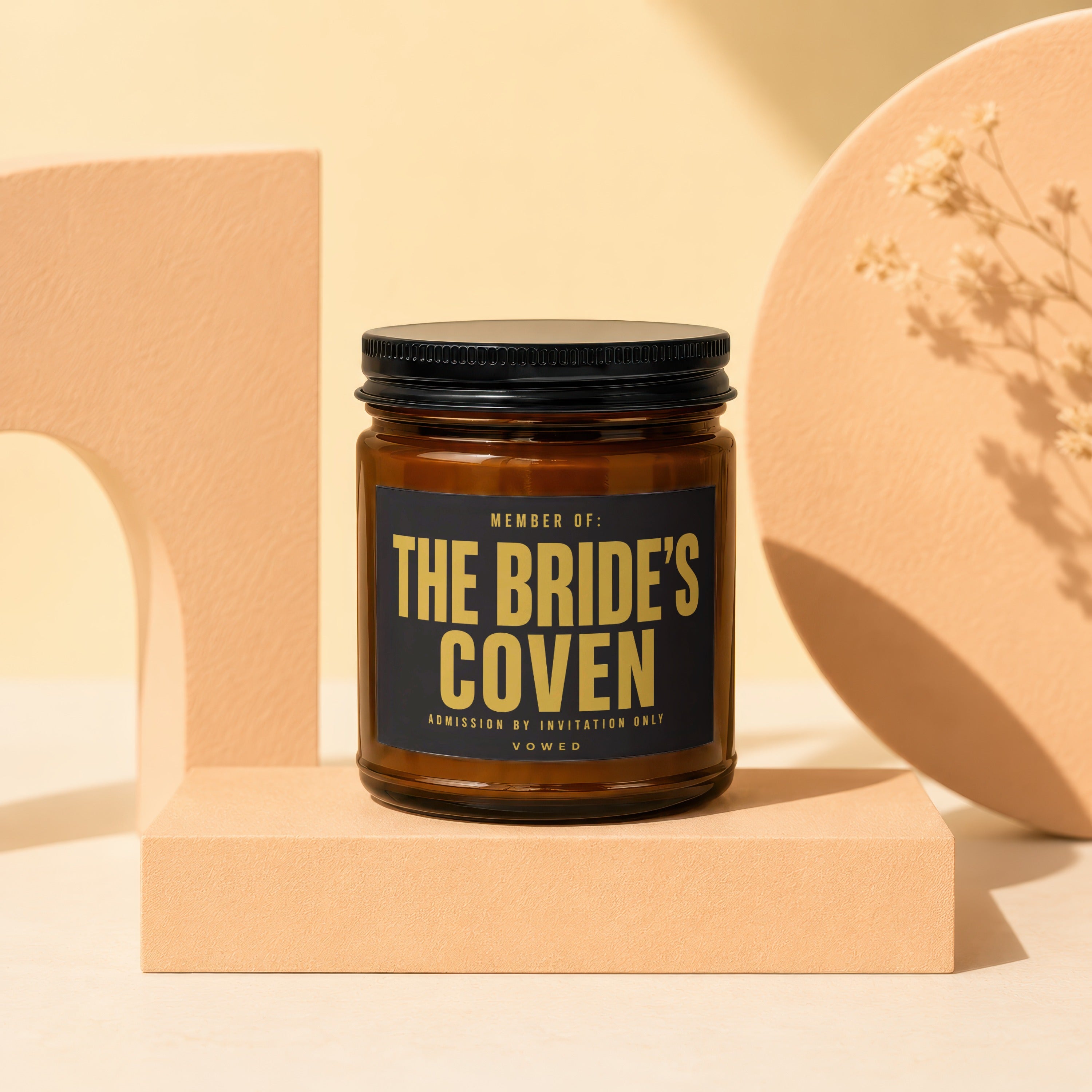 Amber candle with black label reading "MEMBER OF: THE BRIDE'S COVEN ADMISSION BY INVITATION ONLY VOWED."
